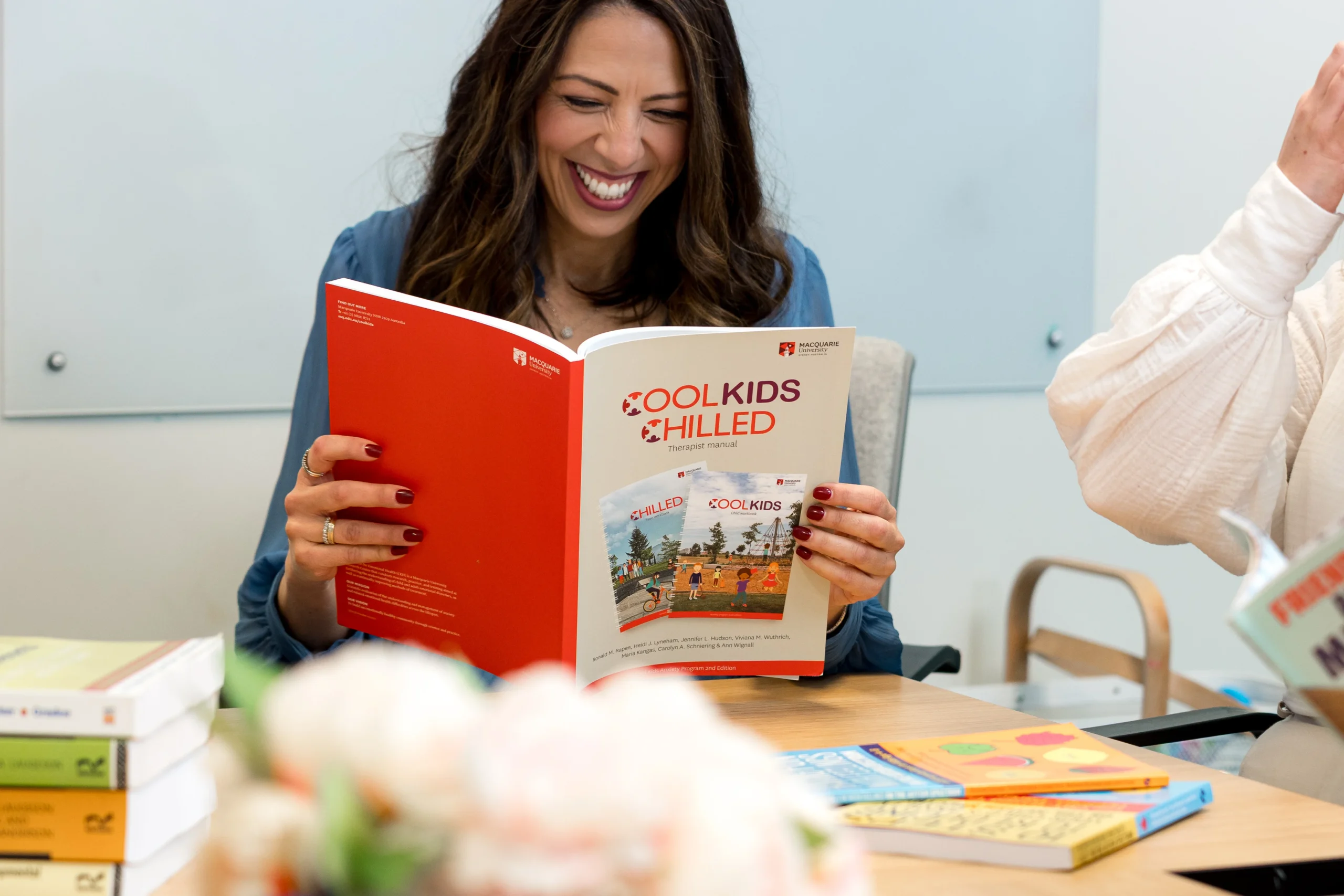 A psychologist laughing while holding the Cool Kids Chilled therapist manual