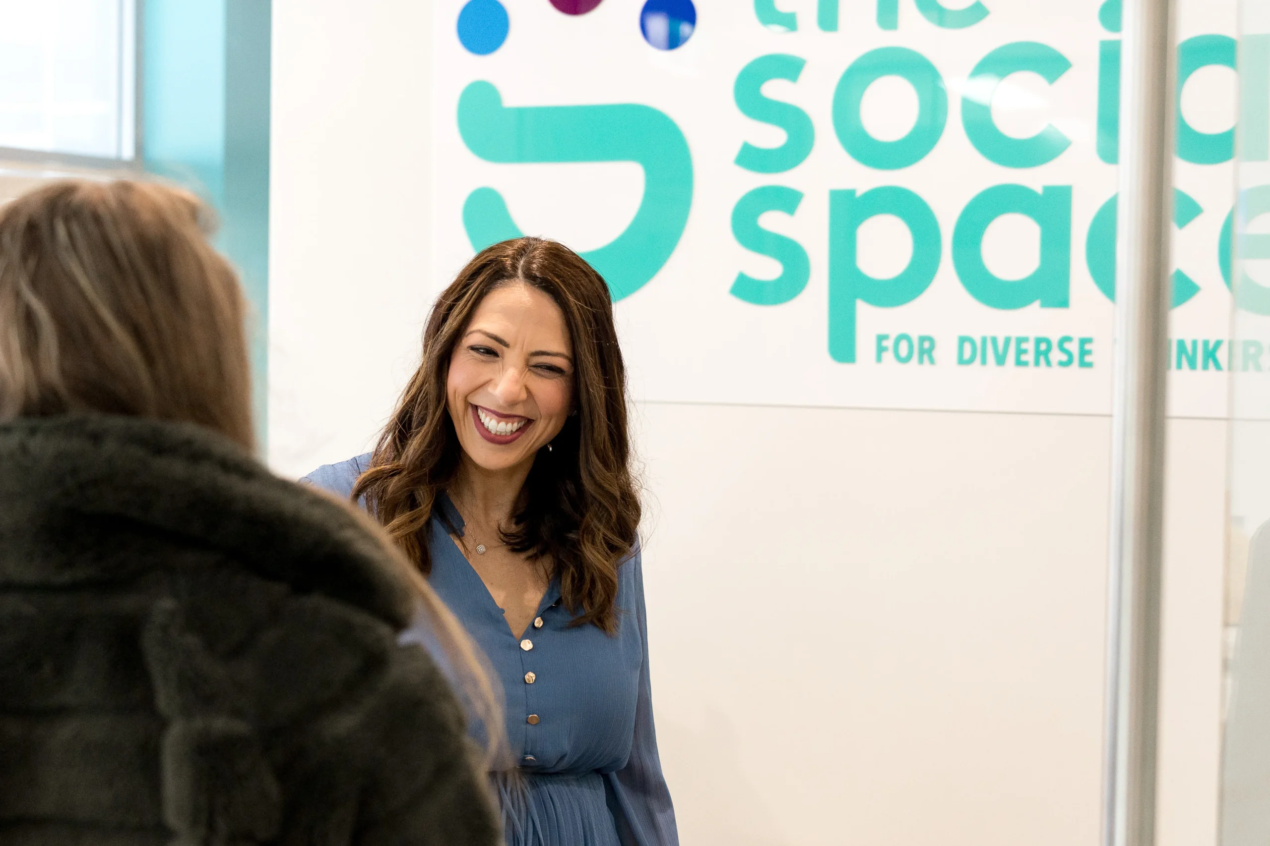 A clinician laughing with a visitor in front of The Social Space sign